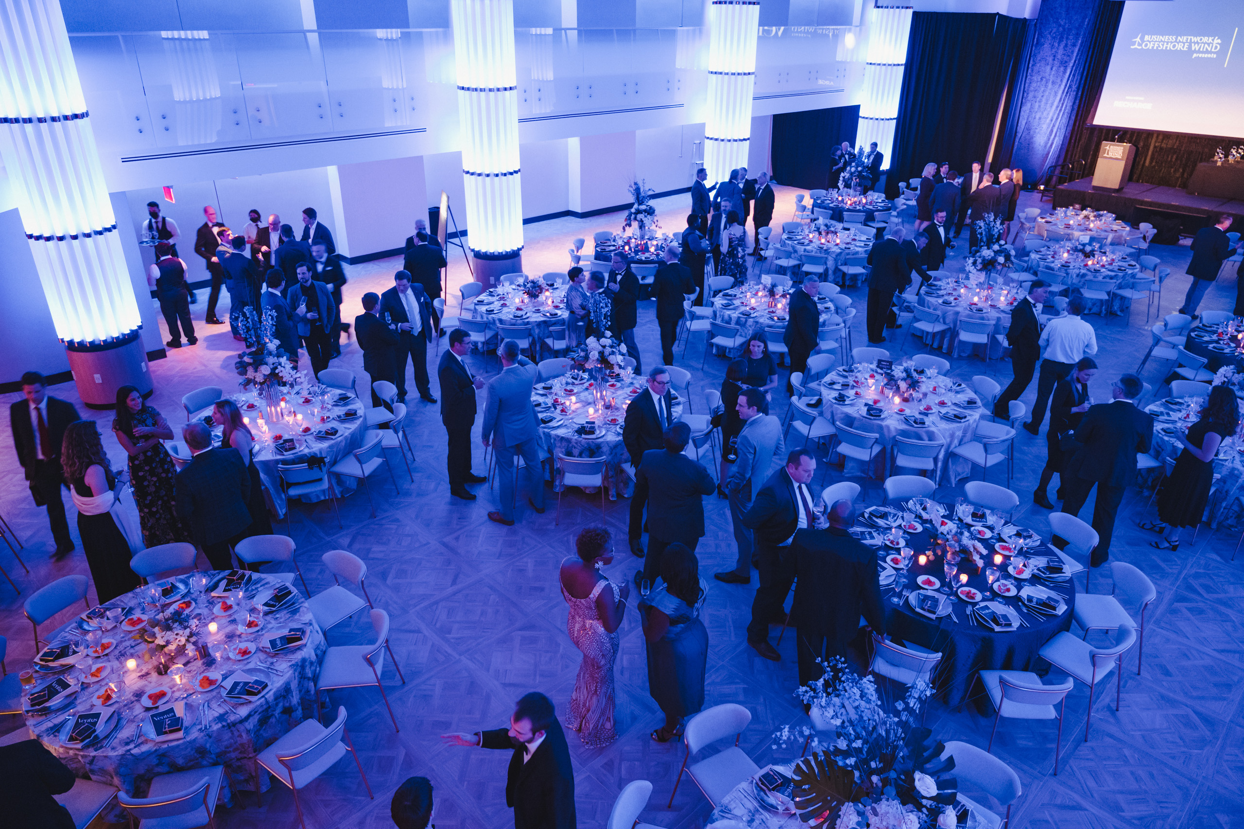 Formal gala with round tables and blue lighting.