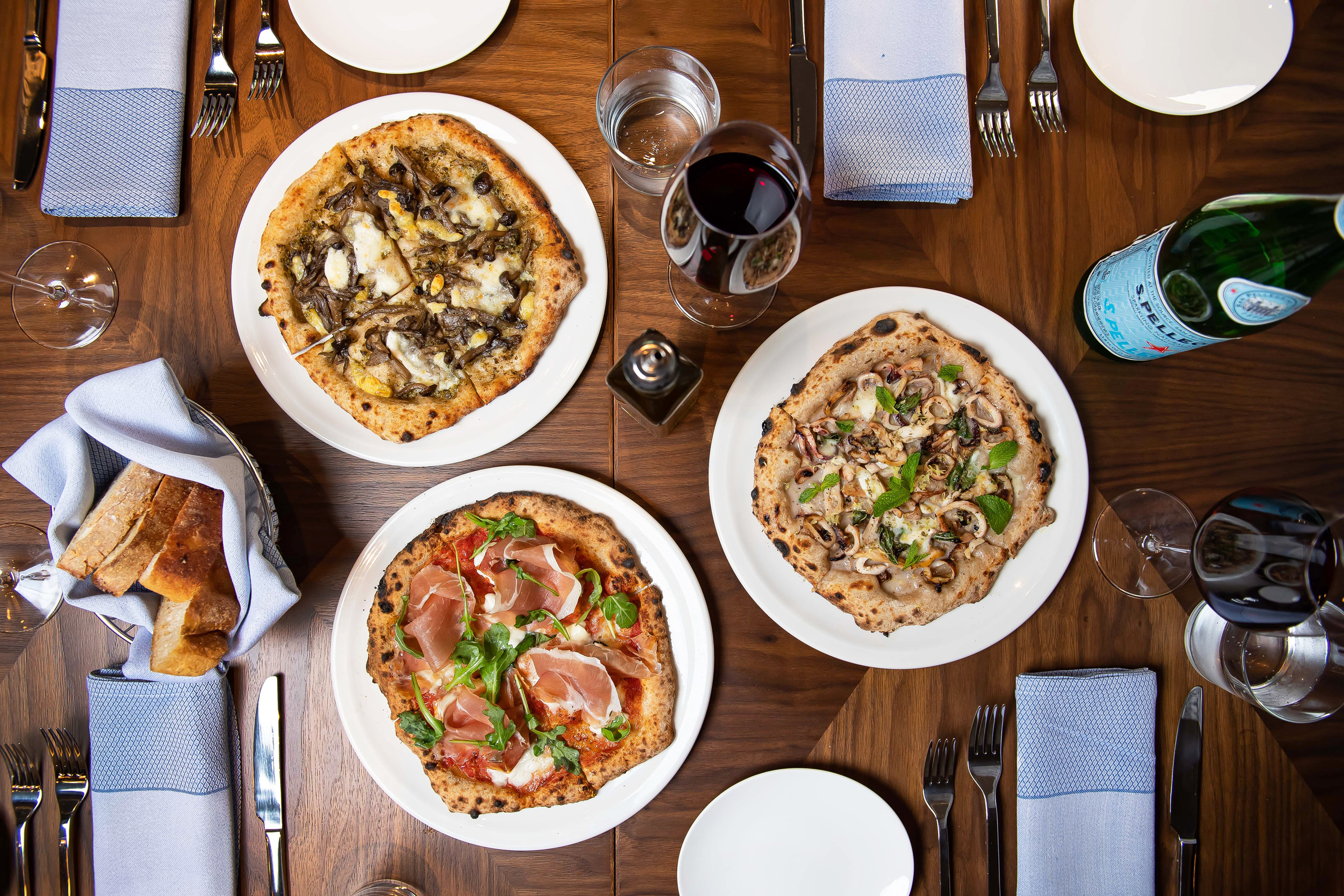 Overhead view of pizzas, wine, and table setting.
