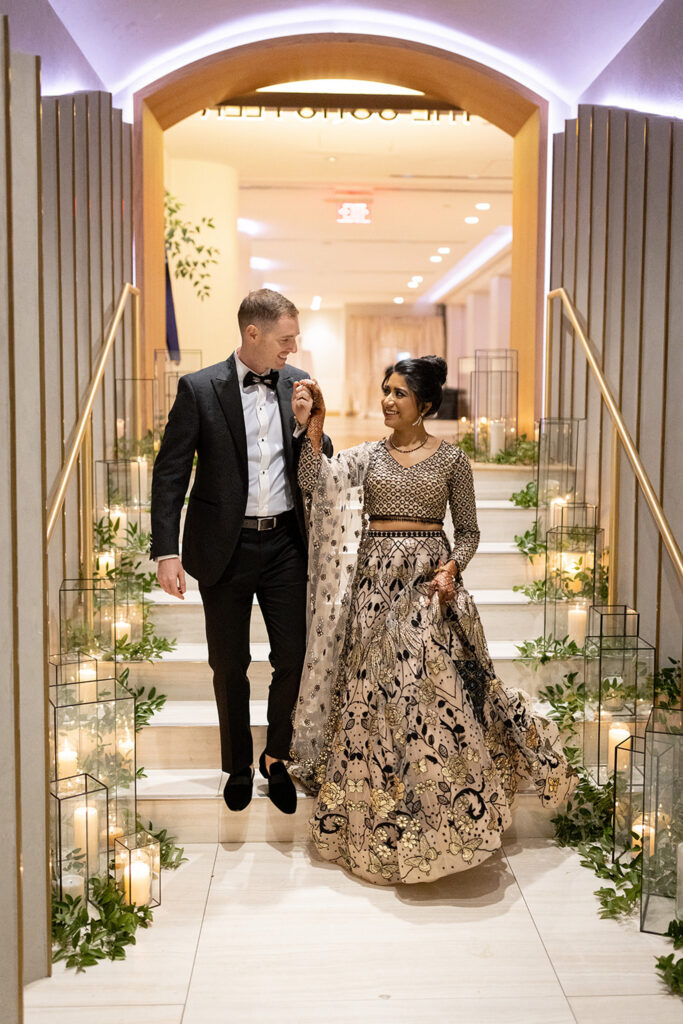 Newlyweds walking through candlelit archway.