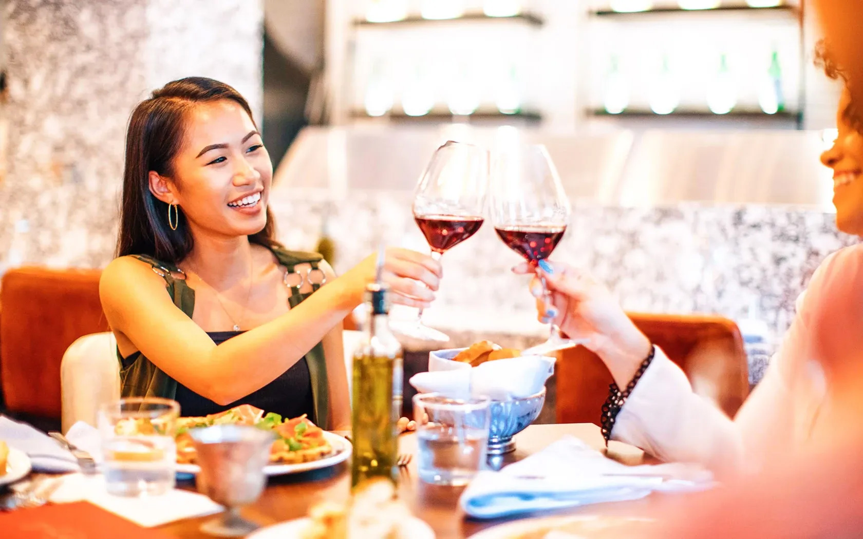 Two women toasting red wine at dinner.
