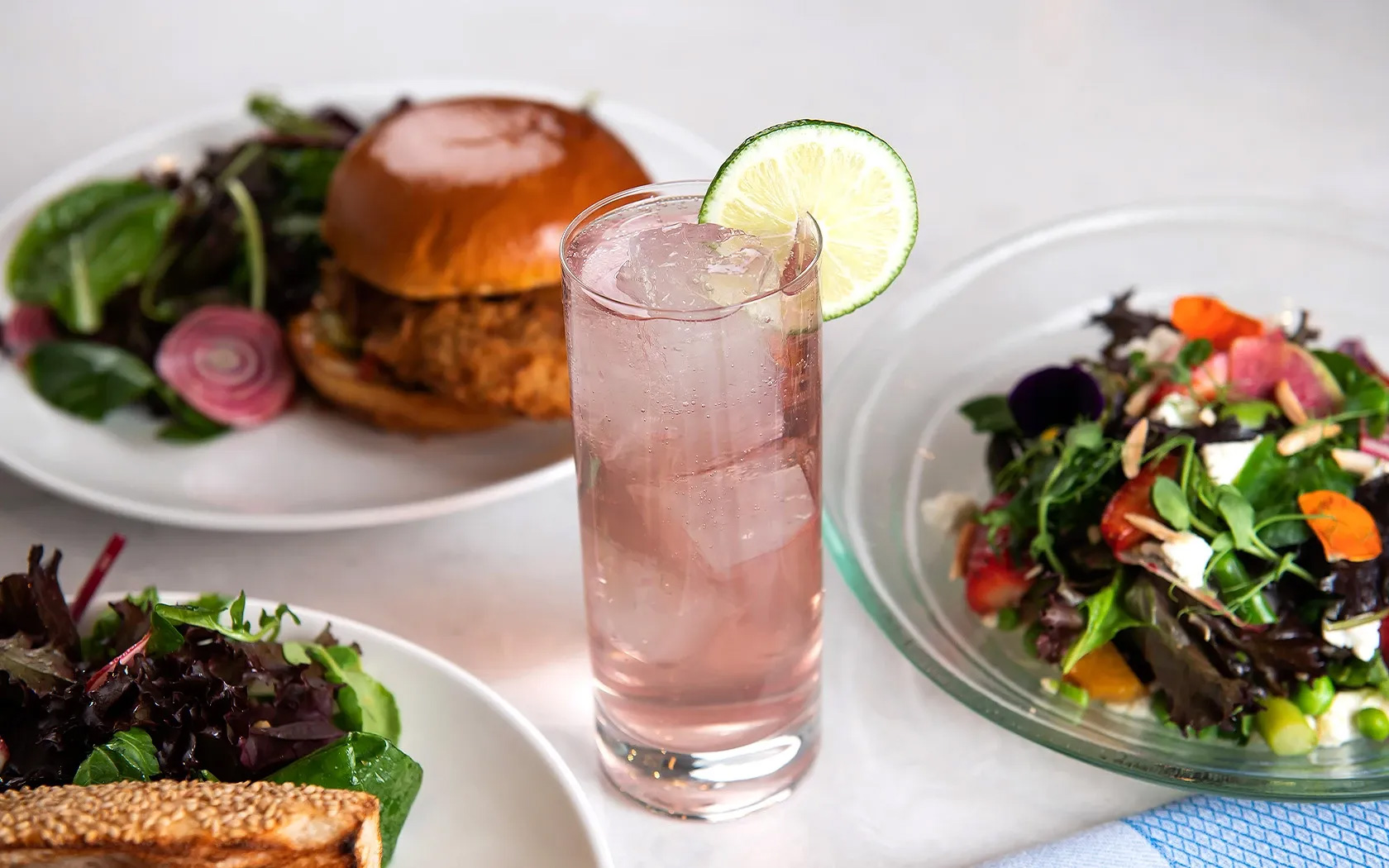 Pink cocktail with burger and fresh salads.