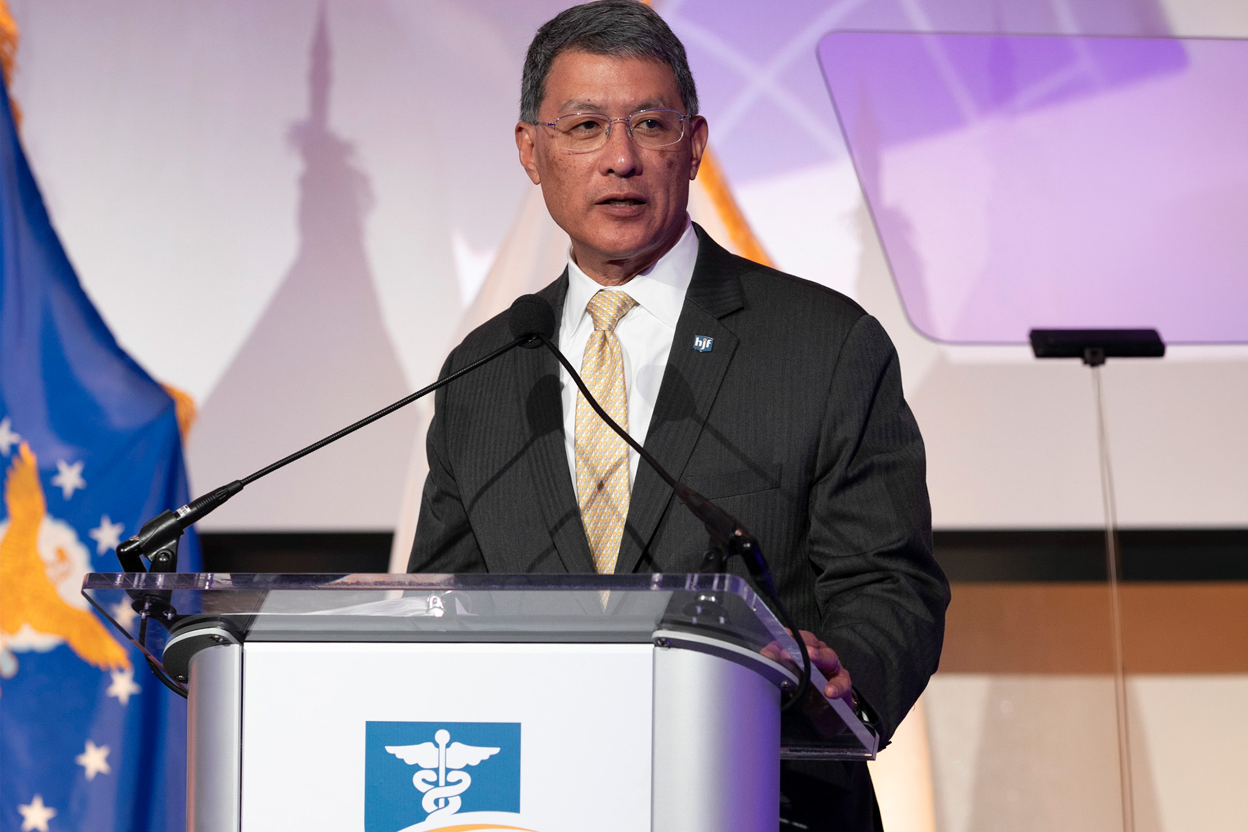 man in suit reading from teleprompter behind a podium