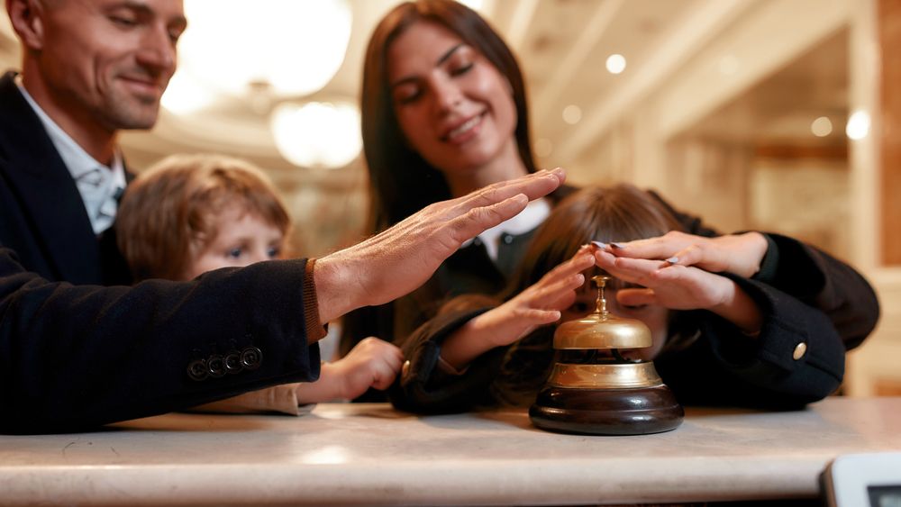 A family stood at a hotel check in counter pressing the bell